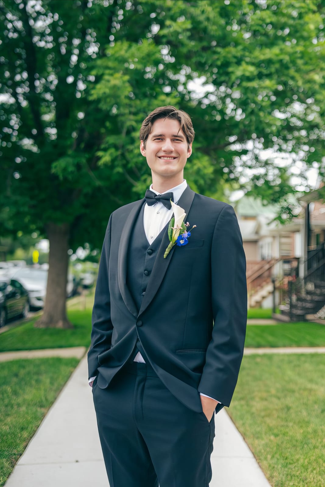 Eric smiling in his tuxedo on a tree-lined sidewalk