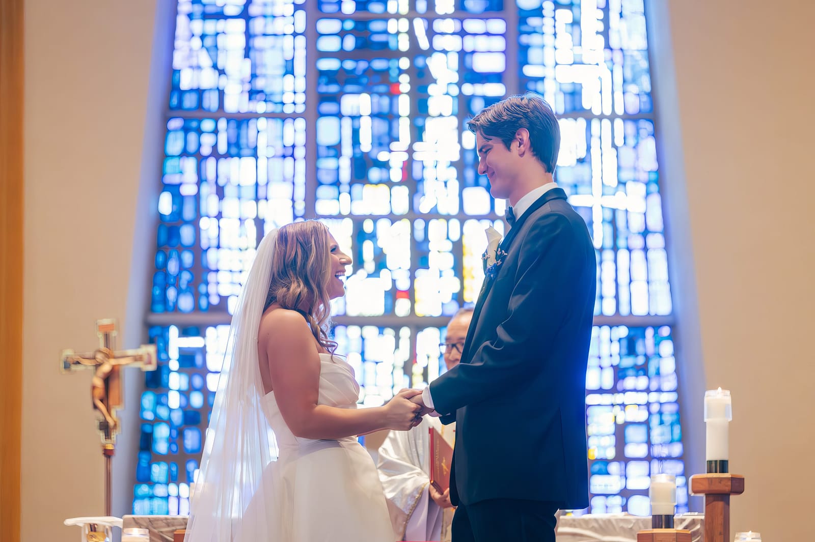 Carol and Eric holding hands at the altar in front of a stained glass window
